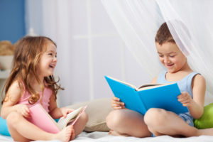 children sitting together on a bed looking at books and giggling