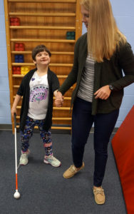 child walking with white cane with physical therapist