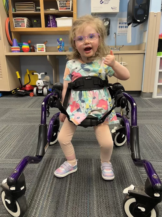 Young girl smiling while using a purple gait trainer